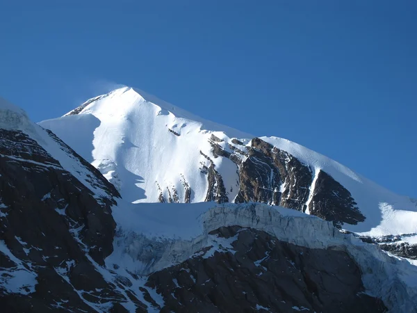 Wind bläst Schnee über einen hohen Berg — Stockfoto