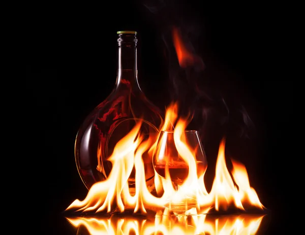 Flasche Cognac in Feuerflamme auf schwarzem Hintergrund — Stockfoto