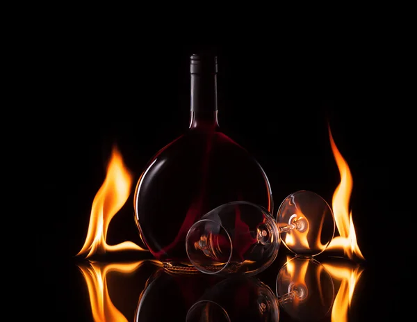 Flasche und Glas Wein in Feuerflamme auf schwarzem Hintergrund — Stockfoto