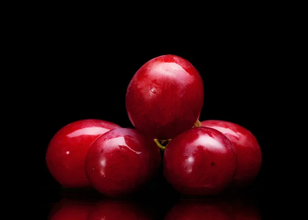 Cacho de uvas vermelhas em um fundo preto com gotas de água — Fotografia de Stock