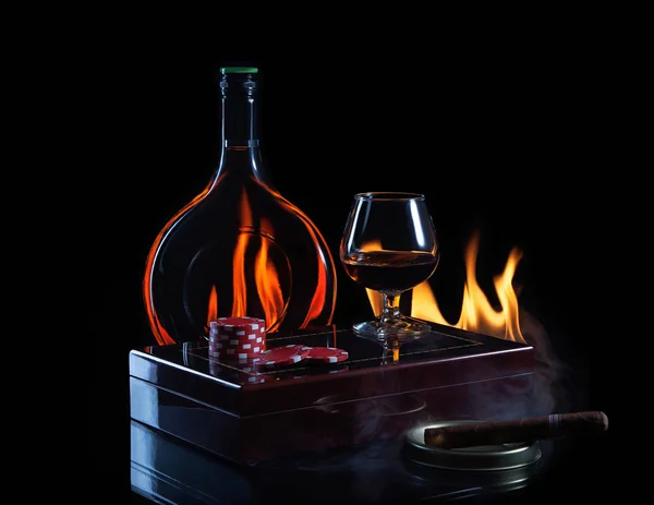 Бутылочный бокал коньяка с покерными маркерами и сигарой в огне — стоковое фото