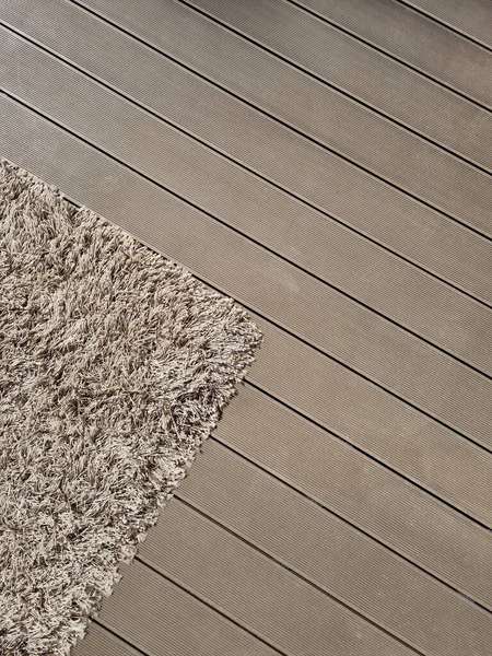 Shaggy carpet on brown wooden floor. Mixed textures in interior. Fluffy rug at the open terrace covered with decking.  Kids\' toy laying on the carpet.