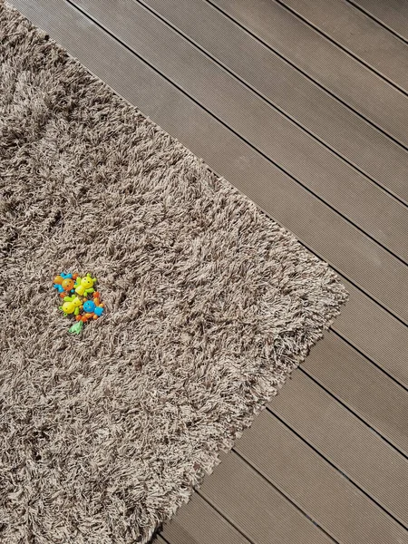 Shaggy carpet on brown wooden floor. Mixed textures in interior. Fluffy rug at the open terrace covered with decking.  Kids\' toy laying on the carpet.