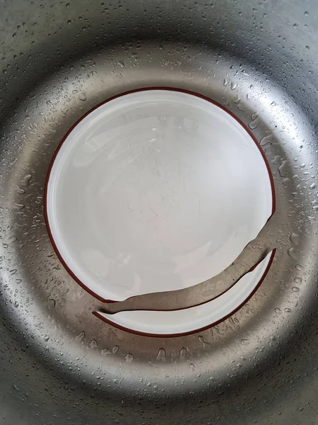 Ceramic plate broke apart. Failure in the kitchen during meal preparation. Dinner plate cracked into pieces. Plate shreds in the sink.