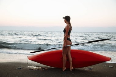 Siyah mayo giyen güzel bir kız gün batımında denizde yüzmek için turuncu bir kanoyla gider.