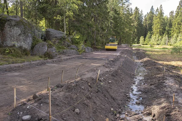 Kazıcı, ormanlık alandaki bir inşaat alanında dağın yamaçlarını güçlendirmek için bir rögar ve ızgara yapmak için bir siper kazıyor. Yokuşta bir yol, drenaj kanalı ve drenaj ızgarası inşaatı
