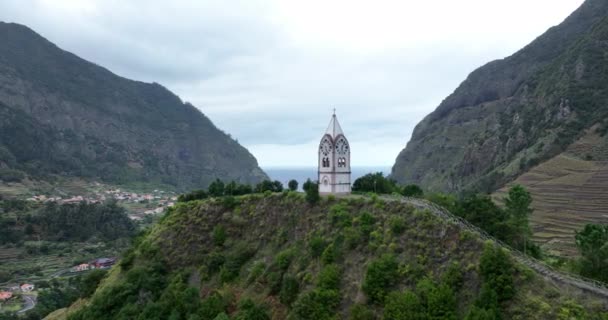 Small church surrounded by cliffs and mountains and a village in a green nature landscape scenery. In Madeira Portugal. — Stock Video