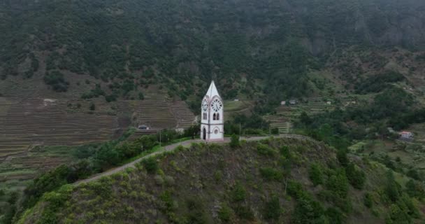 Small church surrounded by cliffs and mountains and a village in a green nature landscape scenery. In Madeira Portugal. — Stockvideo