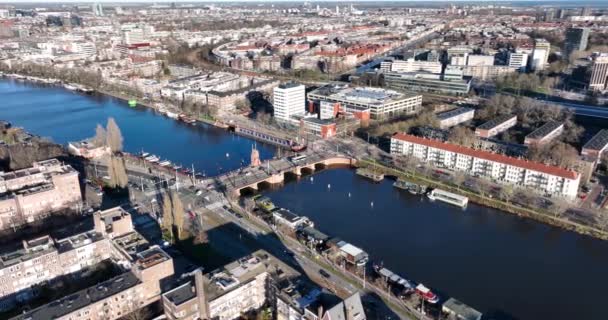 Letecký pohled na Berlage brug v Amsterdamu, Nizozemsko. Infrastruktura přechodu přes řeku Amstel. tramvaj a dopravní přejezd. Pohled na město. — Stock video