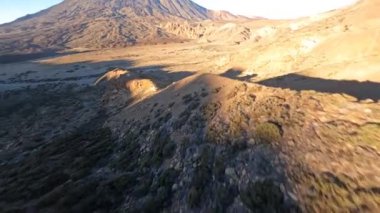 FPV insansız hava aracı, arka planda bir dağ volkanı olan bir arazi gibi çölün üzerinde uçuyor. Uçurumların, kayaların ve bitkilerin üzerinden yakın uçmak doğa.