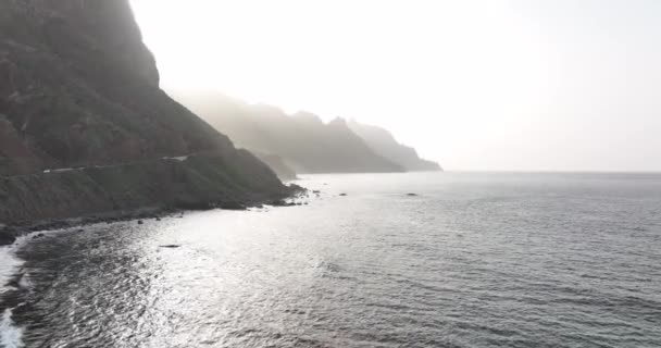 Скалистый вулканический пляж, окруженный высокими горами и скалами с видом на беспилотник. Тенерифе Испания Канарейские острова Европа. — стоковое видео