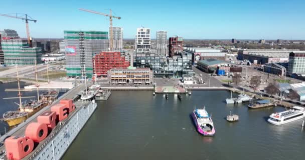 Ámsterdam, 19 de marzo de 2022, Países Bajos. NDSM ferry que llega moderno astillero industrial y zona residencial de moda. GVB Ijveer llegada de pasajeros de transporte público vista aérea de drones. — Vídeo de stock