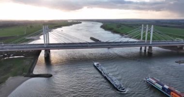 Ewijk, 9 Nisan 2022, Hollanda. Üzerinde otoyol ve trafik olan asma köprü altından geçen ticari ulaşım gemileri. Hava aracı görünümü Günbatımı