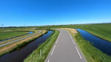Açık asfalt bir yolda köşelerden hızla FPV drone kuadkopteri uçurmak. Açık çayır manzarasında otoyol altyapısı taşımacılığı.