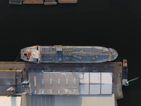 Petrochemical energy heavy transport industry cargo vessel tanker top down aerial drone view. Docked bulk carrier ship along storage facility silos.