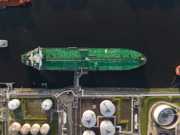 Petrochemical energy heavy transport industry cargo vessel tanker top down aerial drone view. Docked bulk carrier ship along storage facility silos.
