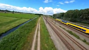 Utrecht, 1st of July 2022, The Netherlands. NS train Nederlandse Spoorwegen FPV drone high speed follow through a grassland landscape. Sustainable travel mobility.