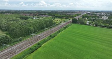 Dutch train passing commuting traveling in forrest grassland nature landscape. Sustainable travel technology by rail road modern railway rialroad transportation.