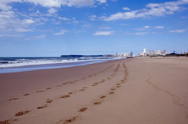 Huellas en la arena con ciudad en la distancia —  Fotos de Stock