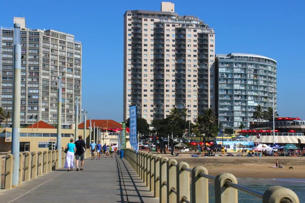 People Walk on Pier Towards City Skyline