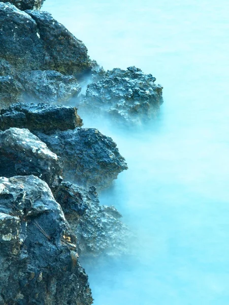 Sharp reef in blue troubled water, salt spray above, noisy waves. — Stock Photo, Image