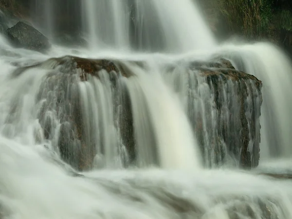 Blick in einen Wasserfall voller Wasser nach starkem Regen. Tropfen fallen auf Felsen und bilden blaue und grüne Gischt. — Stockfoto