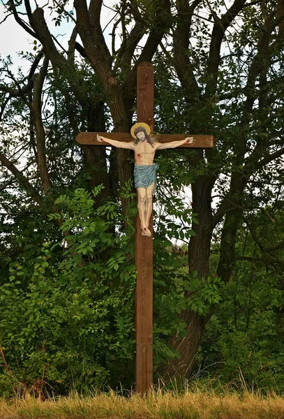 Traditioneel dorp kruisbeeld met geschilderde Jezus in de patch naar de kerk. schaduwen van oude bomen. — Stockfoto