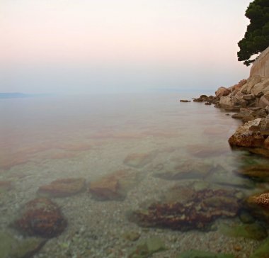 büyük kayanın huzurlu deniz seviyesinden yapışmasını. ufuk yukarıda gökyüzü mavi pembe gündoğumu.