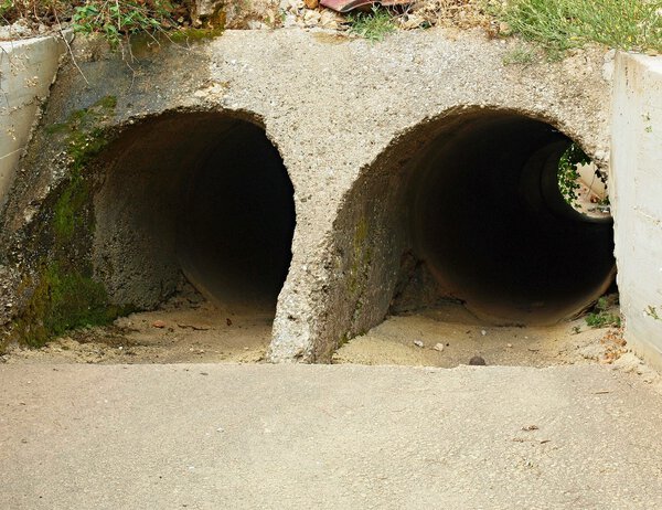 Empty dry drainage channel below town in hot summer period. Concrete bank covered by grass.