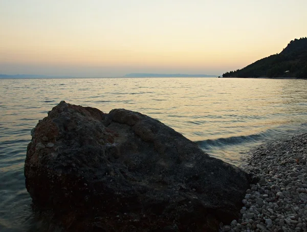 Uma grande pedra está a erguer-se do nível do mar. Céu azul rosa do nascer do sol acima do horizonte . — Fotografia de Stock