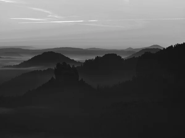 View into deep misty valley in Saxon Switzerland. Sandstone peaks increased from foggy background. Black and white picture. — Stock Photo, Image