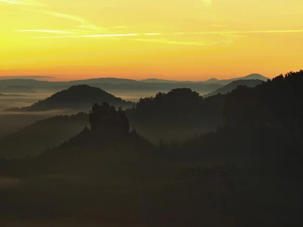 View into deep misty valley in Saxon Switzerland. Sandstone peaks increased from foggy background, the fog is orange due to sunrise. — Stock Photo, Image