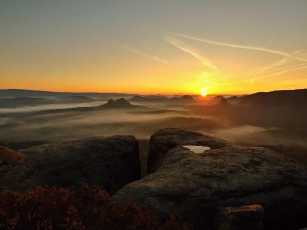 Blick in ein tiefes Nebeltal in der Sächsischen Schweiz. Sandsteingipfel vor nebligem Hintergrund, der Nebel ist orangefarben aufgrund des Sonnenaufgangs. — Stockfoto