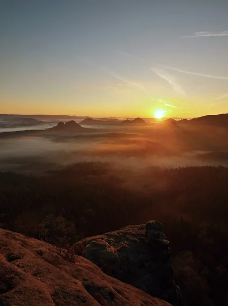 View into deep misty valley in Saxon Switzerland. Sandstone peaks increased from foggy background, the fog is orange due to sunrise. — Stock Photo, Image