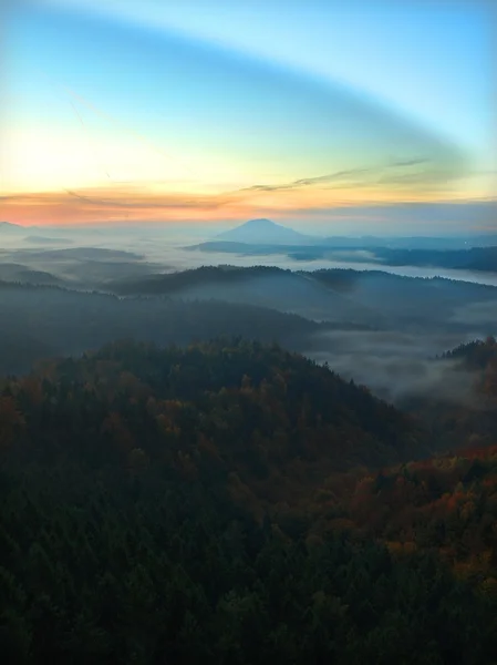 Nascer do sol em uma bela montanha de Checo-Saxônia Suíça. picos de arenito e colinas aumentou a partir de fundo nebuloso, o nevoeiro é laranja devido aos raios de sol . — Fotografia de Stock