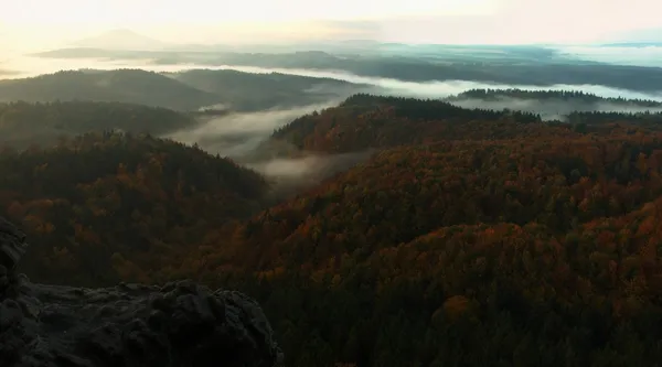 Sunrise in a beautiful mountain of Bohemian-Saxony Switzerland. Sandstone peaks and hills increased from foggy background, the fog is orange due to sun rays. — Stock Photo, Image