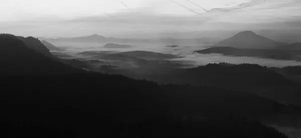 Sunrise in a beautiful mountain of Bohemian-Saxony Switzerland. Sandstone peaks and hills increased from foggy background. First sun rays. Black and White photo. — Stock Photo, Image