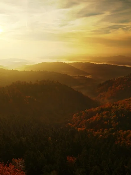 Sunrise in a beautiful mountain of Bohemian-Saxony Switzerland. Sandstone peaks and hills increased from foggy background, the fog is orange due to sun rays. — Stock Photo, Image