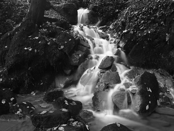 Water spray below small waterfall on mountain stream, water is falling over mossy sandstone boulder. The spray create on level and gravel milky water. — Stock Photo, Image