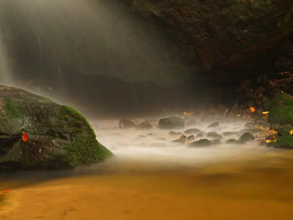 Cascade on small mountain stream, water is running over mossy sandstone boulders and bubbles create on level milky water. Colorful leaves from maple or aspen tree on stones and into water. — Stock Photo, Image