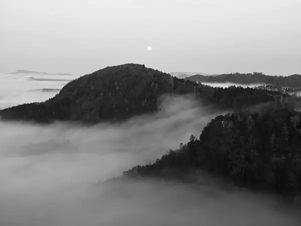 Full moon night with sunrise in a beautiful mountain of Bohemian-Saxony Switzerland. Sandstone peaks and hills increased from foggy background. First sun rays. Black and White photo. — Stock Photo, Image