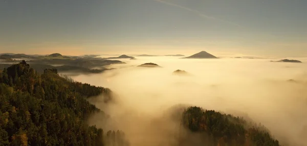 Noite de lua cheia com o nascer do sol em uma bela montanha da Boêmia-Saxônia Suíça. picos de arenito e colinas aumentou a partir de fundo nebuloso, o nevoeiro é laranja devido aos raios de sol . — Fotografia de Stock
