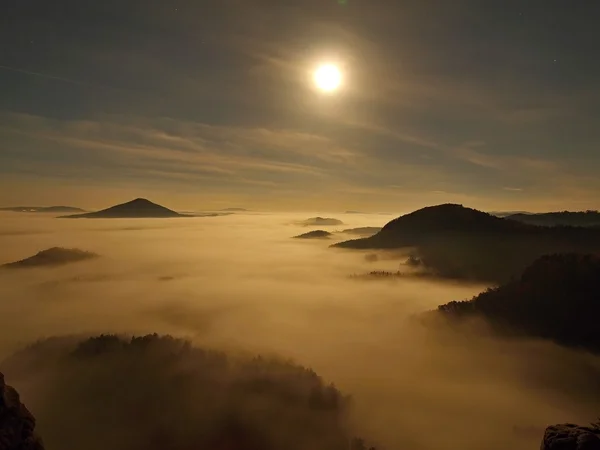 Vollmondnacht mit Sonnenaufgang in einem wunderschönen Berg der böhmisch-sächsischen Schweiz. Sandsteingipfel und Hügel aus dem nebligen Hintergrund verstärkt, der Nebel ist orange aufgrund der Sonnenstrahlen. — Stockfoto