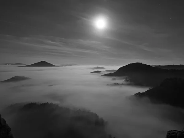 Nuit de pleine lune avec lever de soleil dans une belle montagne de Bohême-Saxe Suisse. Les sommets et les collines de grès ont augmenté à partir du fond brumeux. Premiers rayons du soleil. Photo en noir et blanc . — Photo