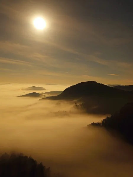 Noite de lua cheia com o nascer do sol em uma bela montanha da Boêmia-Saxônia Suíça. picos de arenito e colinas aumentou a partir de fundo nebuloso, o nevoeiro é laranja devido aos raios de sol . — Fotografia de Stock