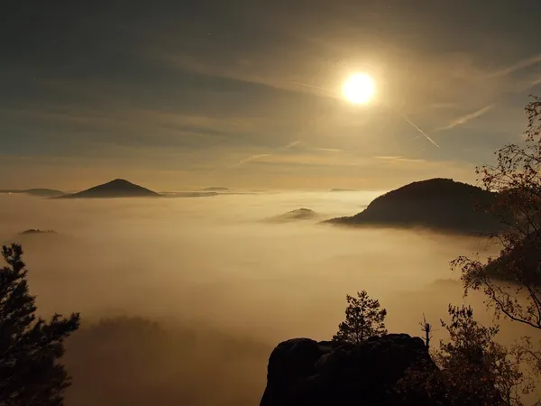 Full moon night with sunrise in a beautiful mountain of Bohemian-Saxony Switzerland. Sandstone peaks and hills increased from foggy background, the fog is orange due to sun rays. — Stock Photo, Image