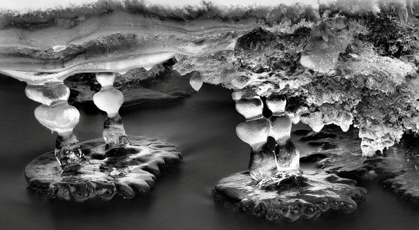 Vista nocturna de invierno a los carámbanos en ramitas y rocas heladas por encima de la corriente rápida. Reflejos de la lámpara de cabeza en carámbanos. Foto en blanco y negro . —  Fotos de Stock