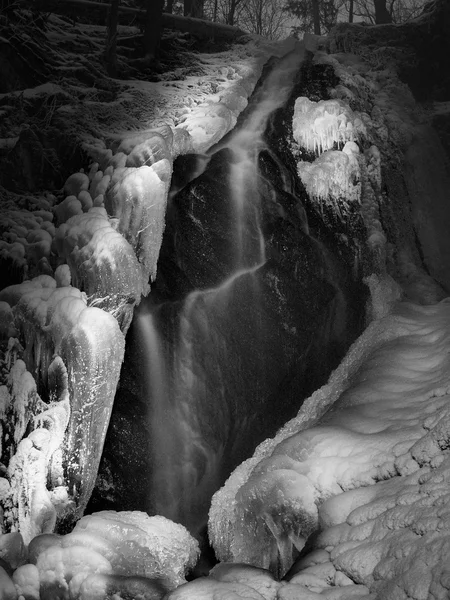 Nacht Winter Blick auf gefrorene Kaskade von Wasserfall, eisige Zweige und eisige Felsbrocken in gefrorenem Schaum des schnellen Stroms. Lichtreflexe in Eiszapfen. Schwarz-Weiß-Foto. Extremer Frost. — Stockfoto