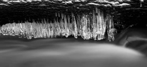 Night winter view to icicles on twigs and icy boulders above rapid stream. Reflections of head lamp in icicles. Black and white photo. — Stock Photo, Image