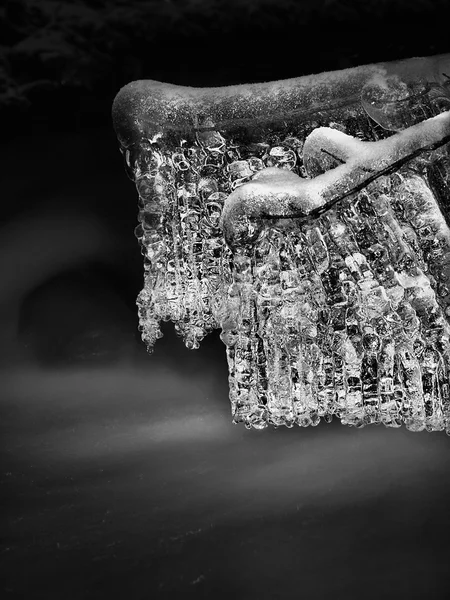 Vista nocturna de invierno a los carámbanos en ramitas y rocas heladas por encima de la corriente rápida. Reflejos de la lámpara de cabeza en carámbanos. Foto en blanco y negro . — Foto de Stock